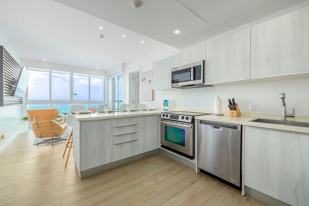 Your bright, fully-equipped kitchen flows seamlessly into the living area, framed by floor-to-ceiling windows revealing stunning ocean views just beyond.