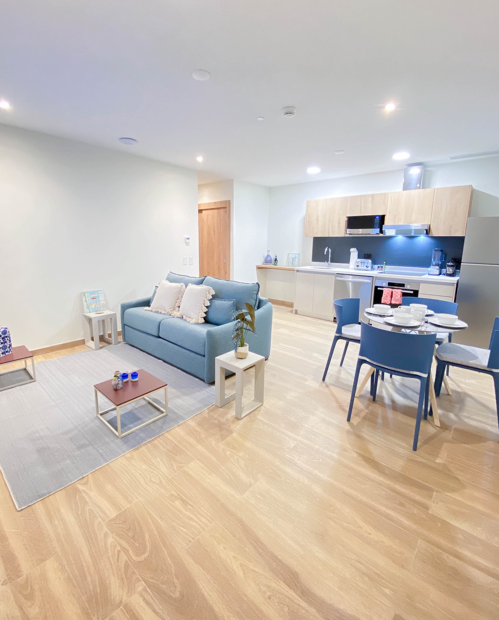 Unwind in your stylish open-plan living space featuring a cozy blue sofa, modern kitchen, and elegant dining area with warm wood floors.
