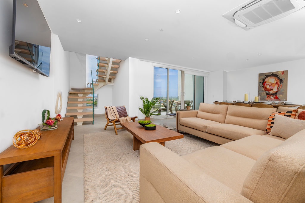 Relax in your bright, art-filled living space with sleek modern furniture, a cozy seating area, and stunning views through floor-to-ceiling windows.