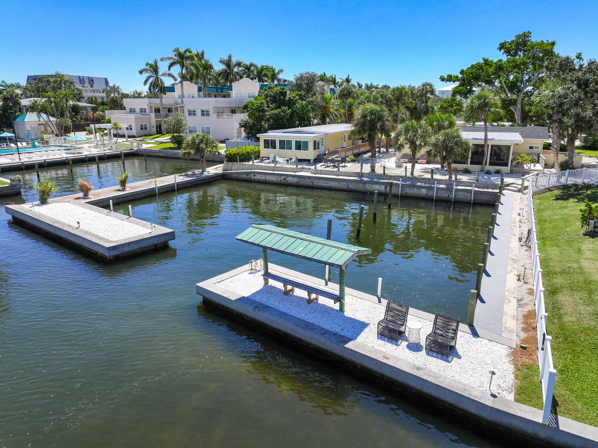 The property features a private waterfront with docks and a covered seating platform on the canal, perfect for fishing or relaxing by the water. Located in a tropical residential neighborhood with palm trees and access to the Intracoastal waterway.