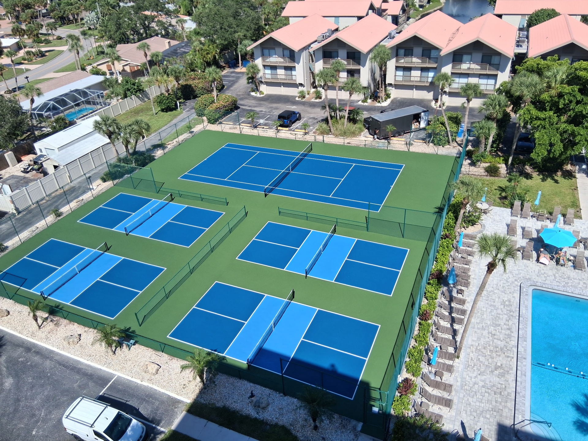 Four pristine tennis courts await alongside a sparkling pool, framed by tropical palms and comfortable loungers—an ideal setting for active days and relaxing afternoons at this Florida-style resort community.