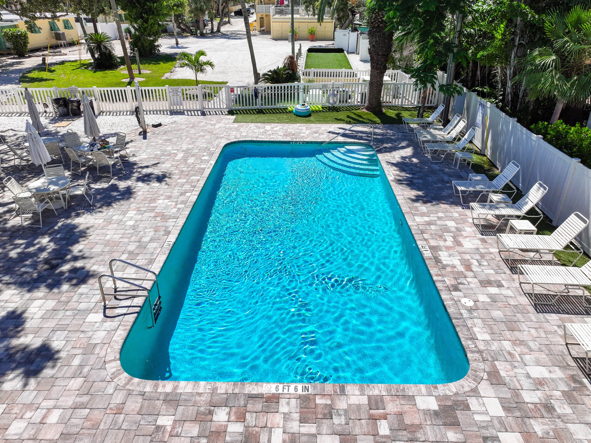 Aerial view of the shared pool area, featuring paver decking, lounge chairs, and lush tropical landscaping surrounding the property.
