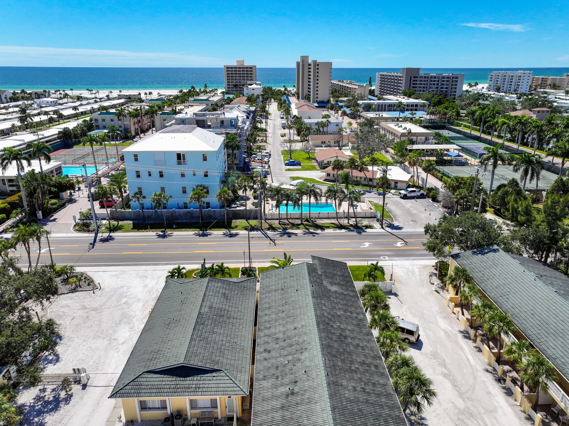 Aerial view of a coastal beach town showing palm-lined streets, residential neighborhoods, and beachfront properties under clear sunny skies.