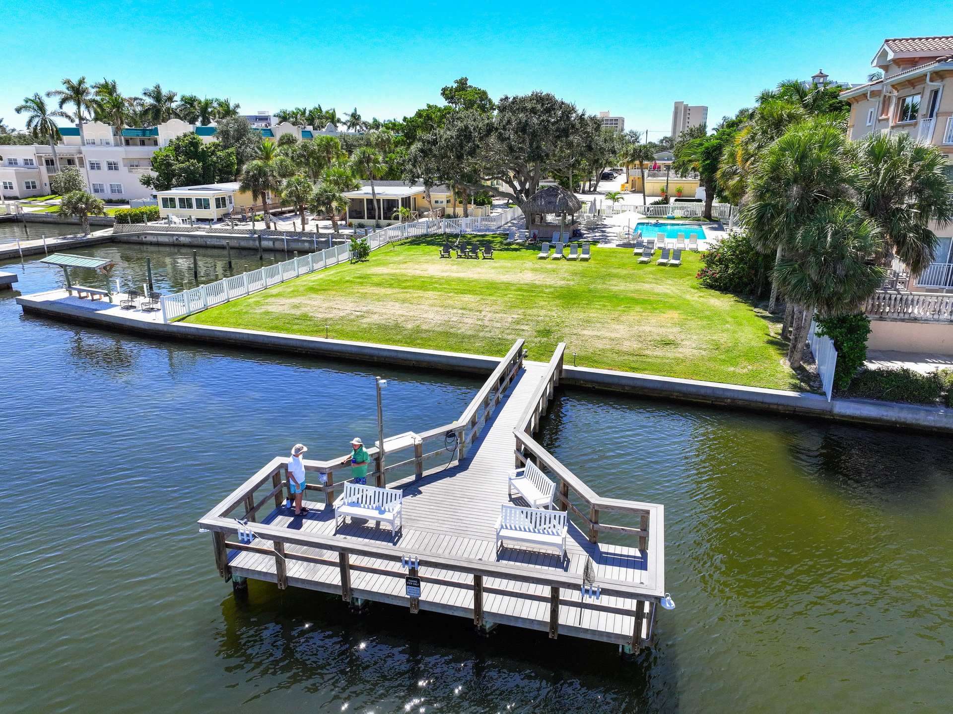 Aerial view of waterfront property featuring private dock on the canal, expansive lawn, and nearby access to local surroundings under clear blue skies.