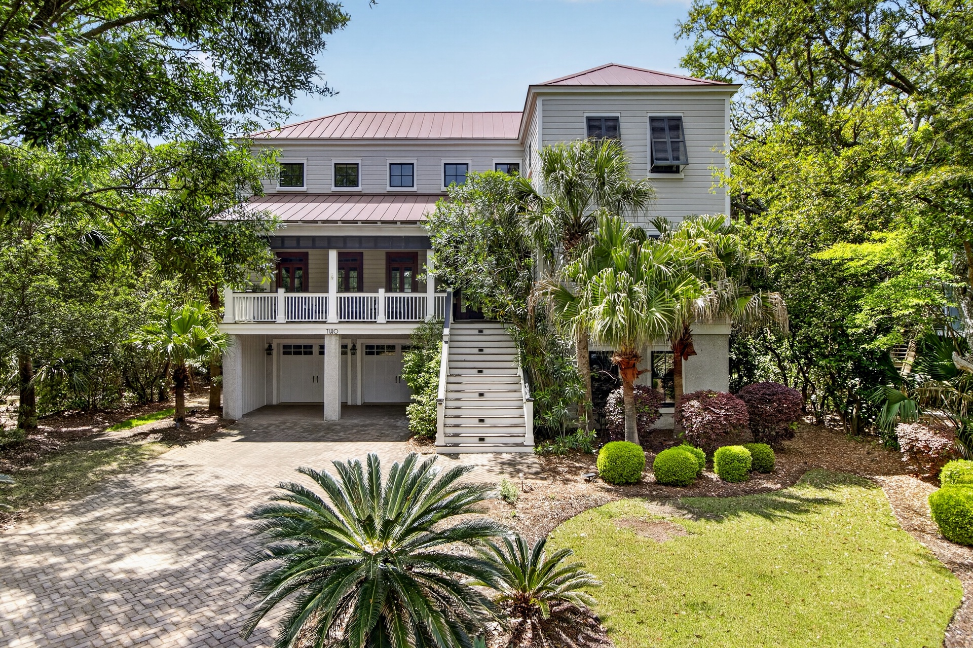 Elegant coastal home with mature tropical landscaping and covered parking nestled among towering trees.