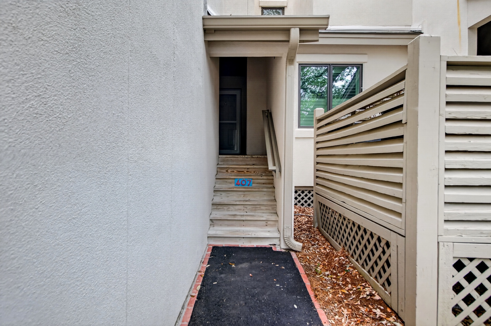 The property entrance is accessed via wooden stairs leading to the front door, marked with unit number 407, surrounded by clean stucco exterior and privacy fencing.