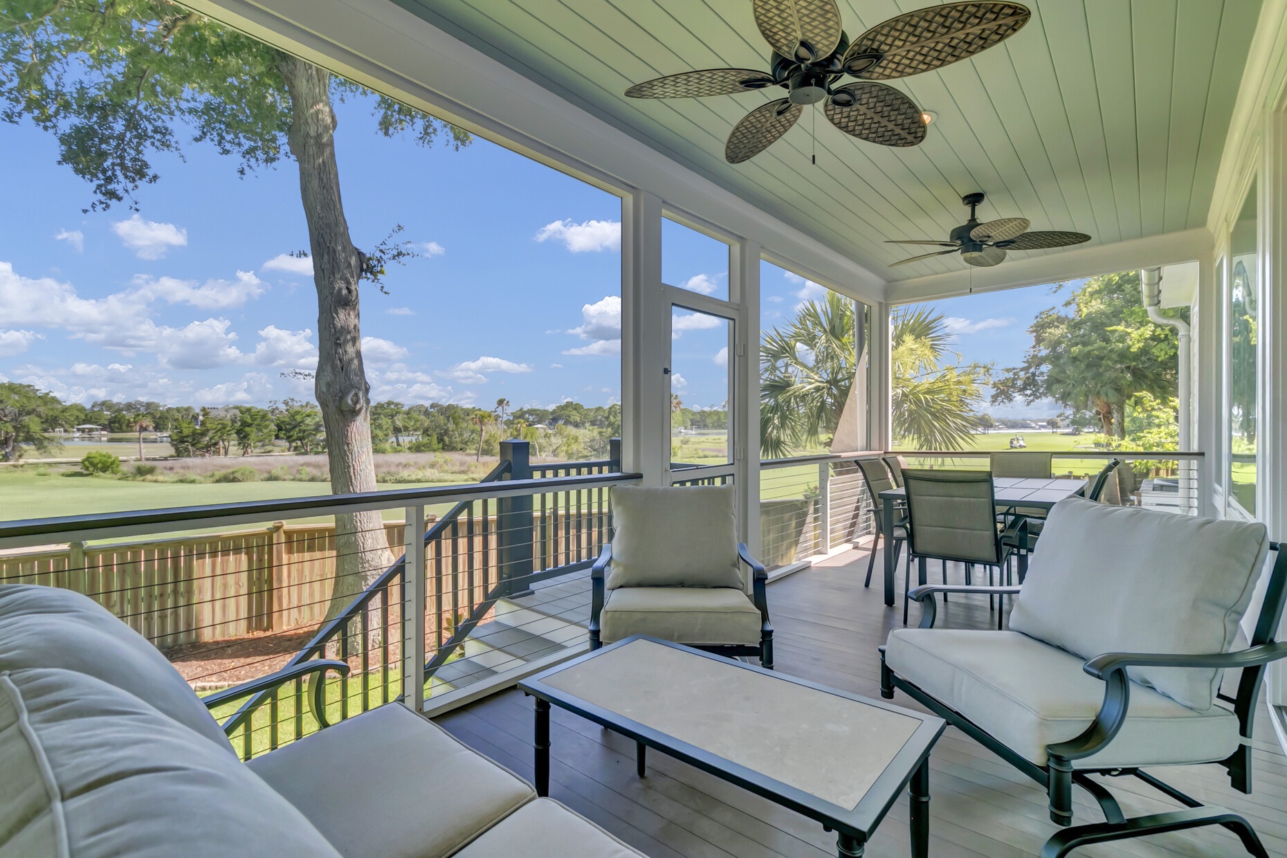 A screened porch with comfortable seating overlooks a golf course and natural landscape, offering a peaceful spot to relax and enjoy the view.