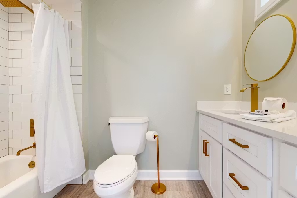 Your elegant bathroom awaits with crisp white subway tiles, warm wood floors, and gold accents creating a spa-like retreat.