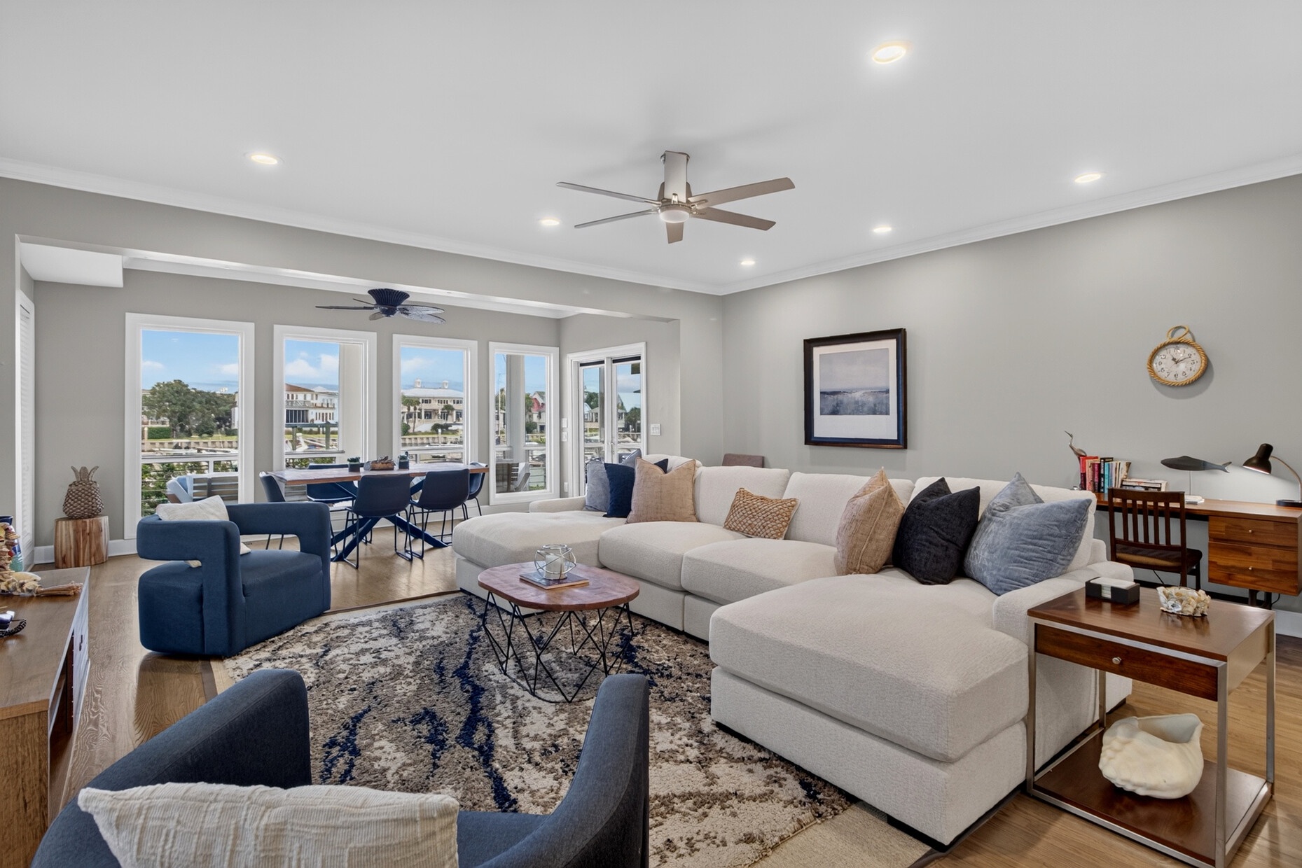 Bright living space with expansive windows flooded with natural light, ceiling fan, and spacious sectional. Relax with stunning marina views from this waterside retreat.