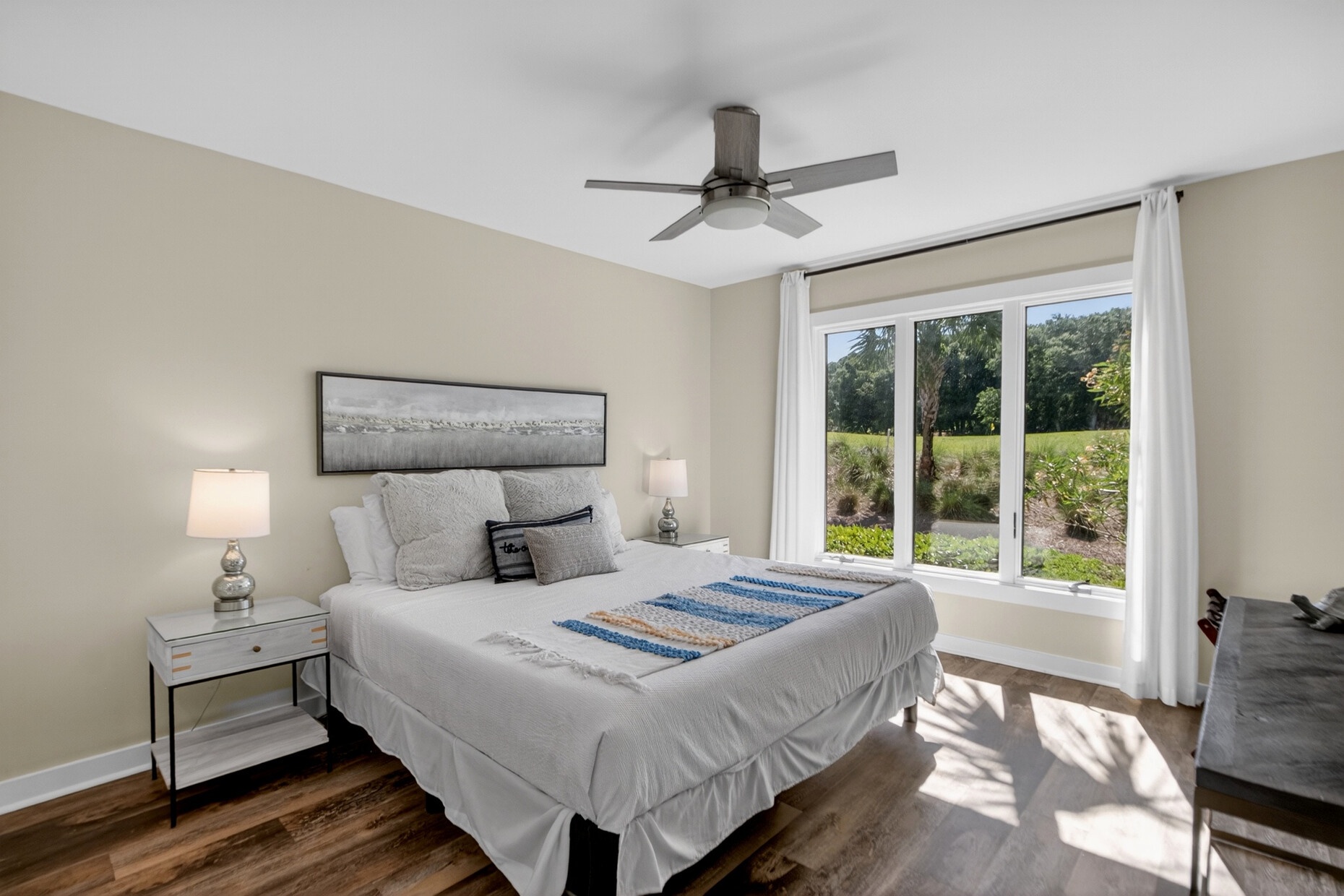 Your serene bedroom features a plush bed, calming neutral tones, and bright natural light from large windows overlooking lush greenery.