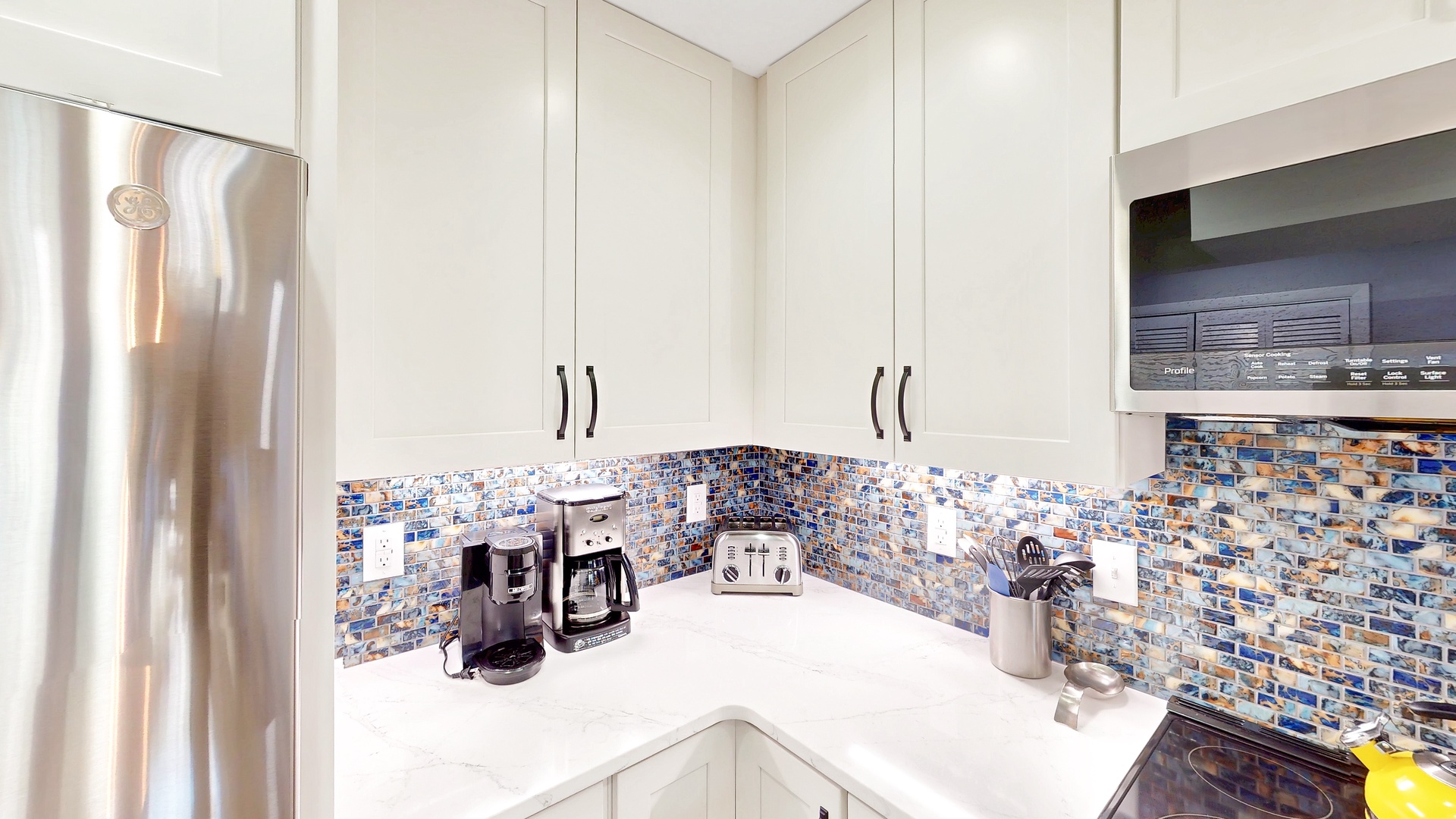Your fully equipped kitchen features gleaming white cabinetry, a mosaic tile backsplash, and modern appliances ready for morning coffee or preparing meals during your stay.