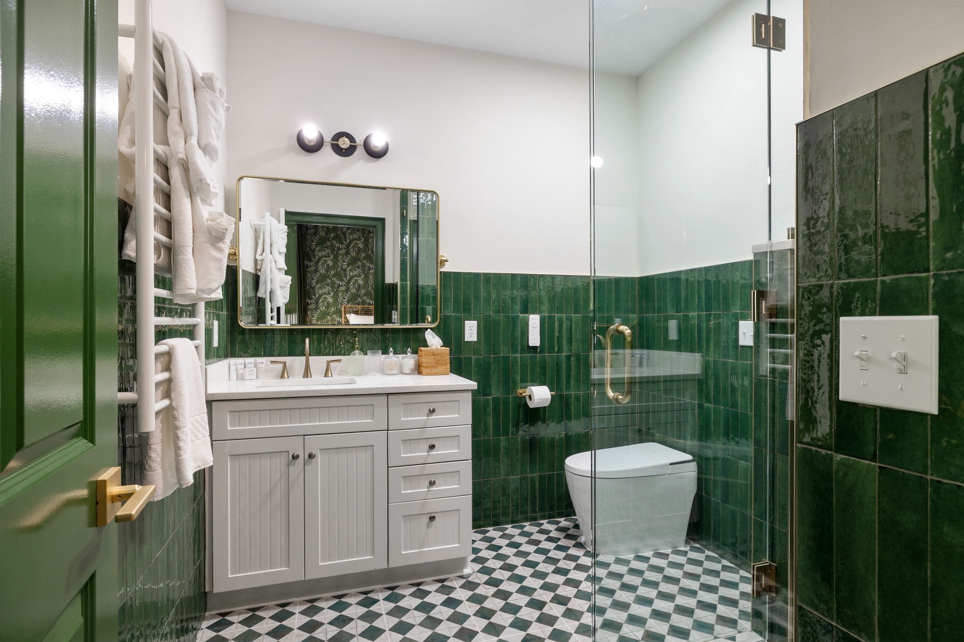 Step into your elegant emerald-tiled bathroom where classic checkered floors meet modern comfort and luxury touches await.