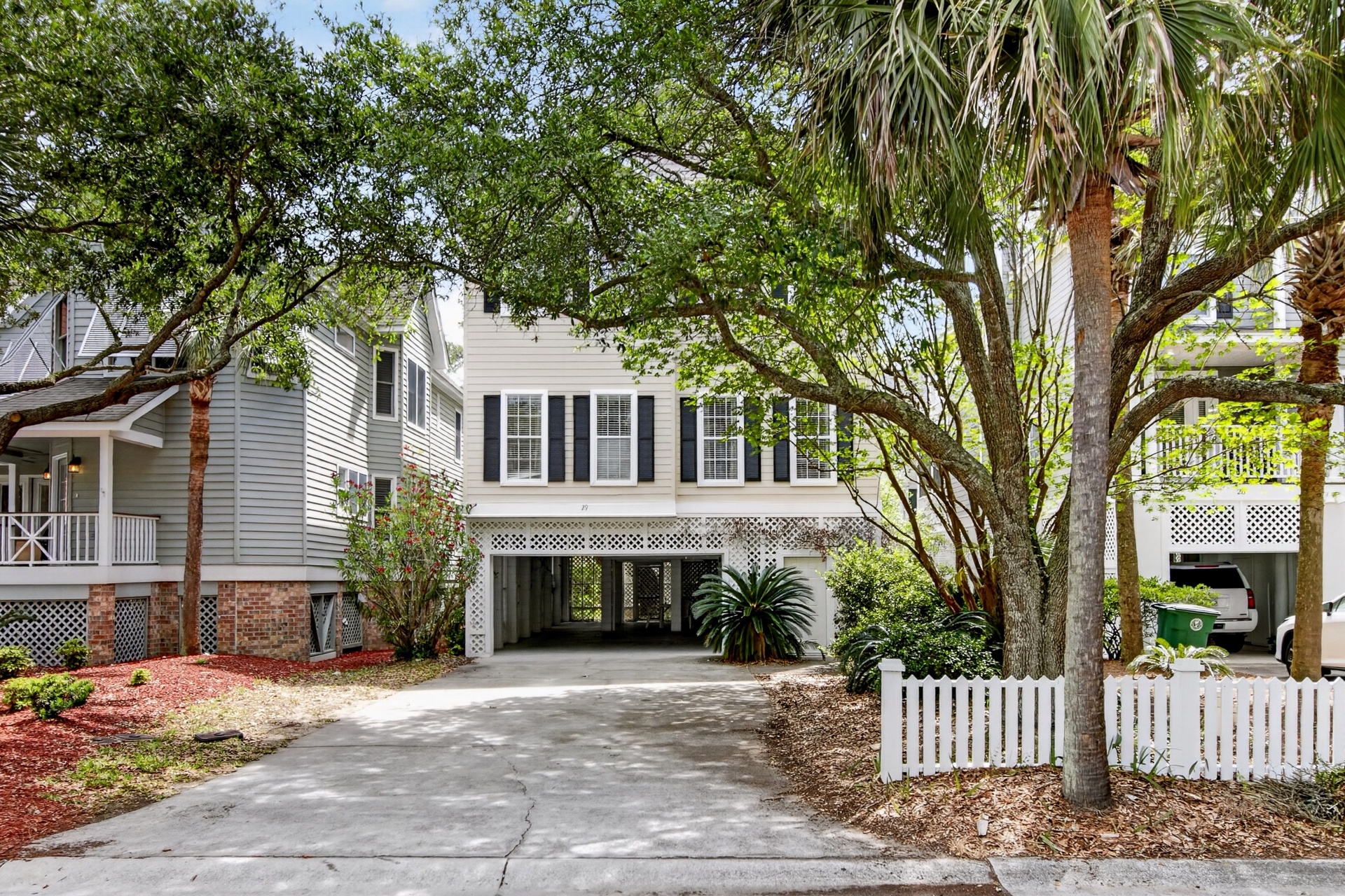 Classic coastal home framed by lush oak trees and palms, offering covered parking and a peaceful neighborhood setting for your beach getaway.