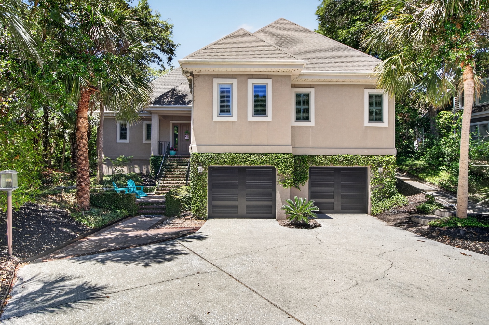 A coastal-style home with two-car garage, nestled among palm trees and lush tropical landscaping in a quiet neighborhood setting.