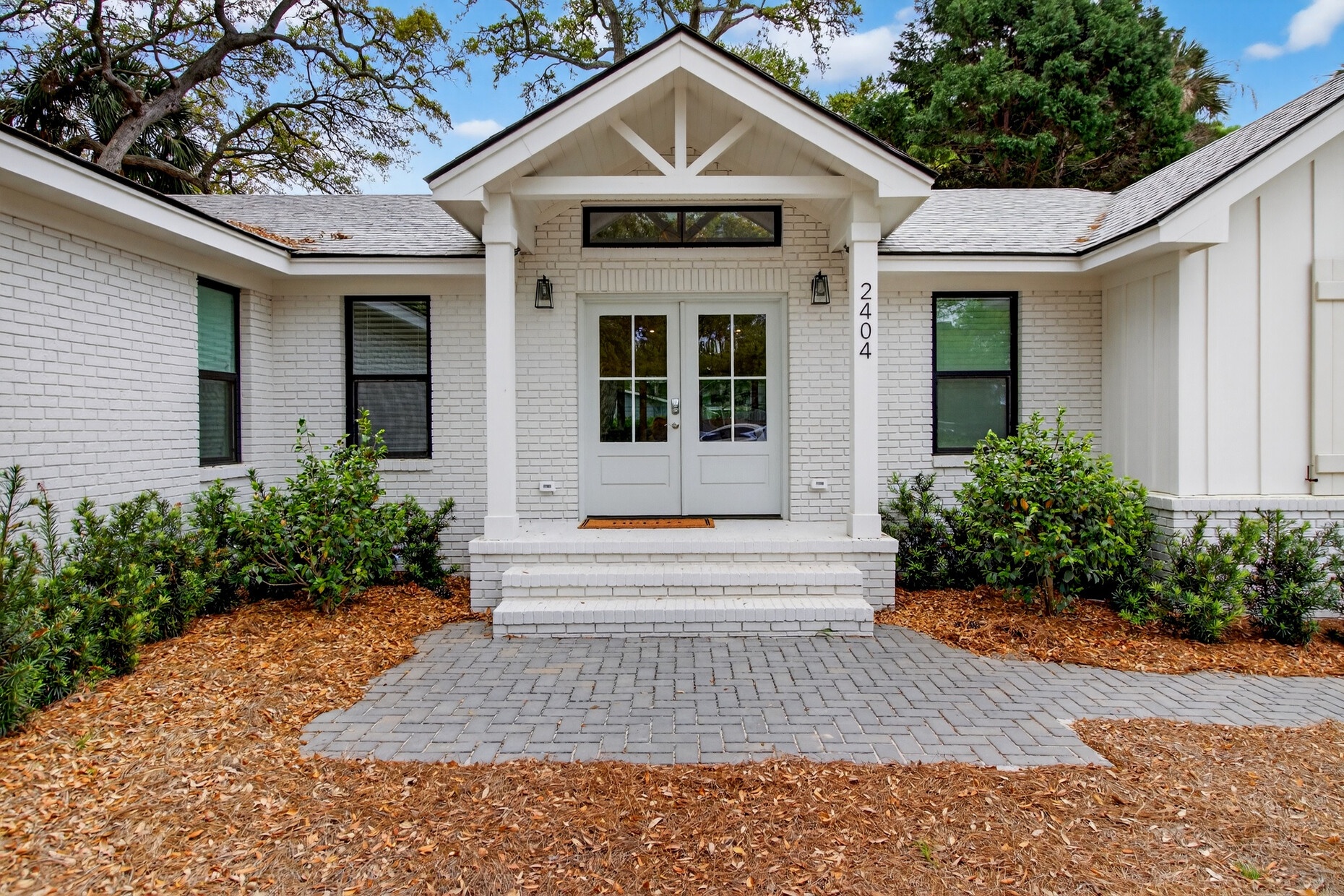 Charming white brick home features a welcoming entrance with modern farmhouse details and mature landscaping in a peaceful neighborhood setting.