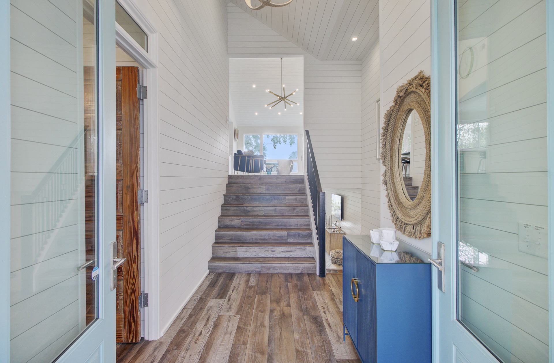 Welcoming entrance hallway with rustic wood stairs leading to your upstairs retreat, featuring coastal-inspired design and natural light.