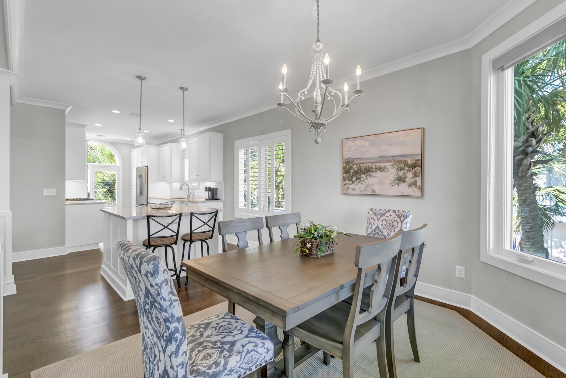 Picture yourself sharing meals at this elegant dining table, bathed in natural light from large windows, while an open kitchen invites easy conversation. The chandelier adds a touch of charm, making every gathering feel special.