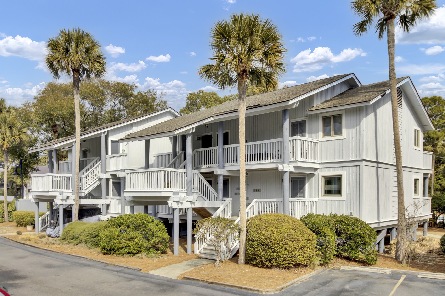 This coastal property features classic gray siding and multiple balconies surrounded by iconic palm trees in a peaceful residential setting.