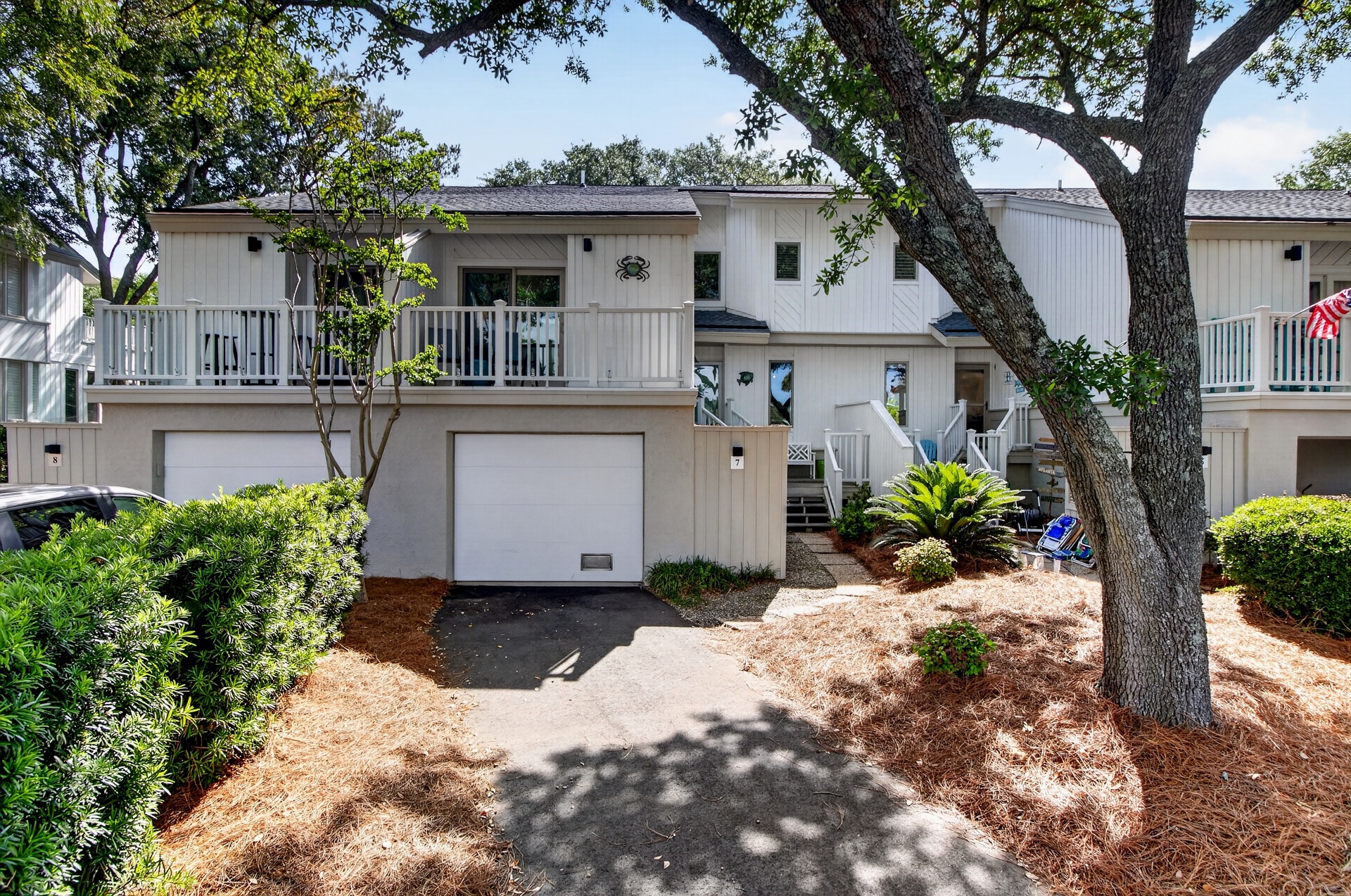This two-story vacation rental features a private garage and inviting balcony, nestled beneath towering oak trees in a peaceful, landscaped setting.