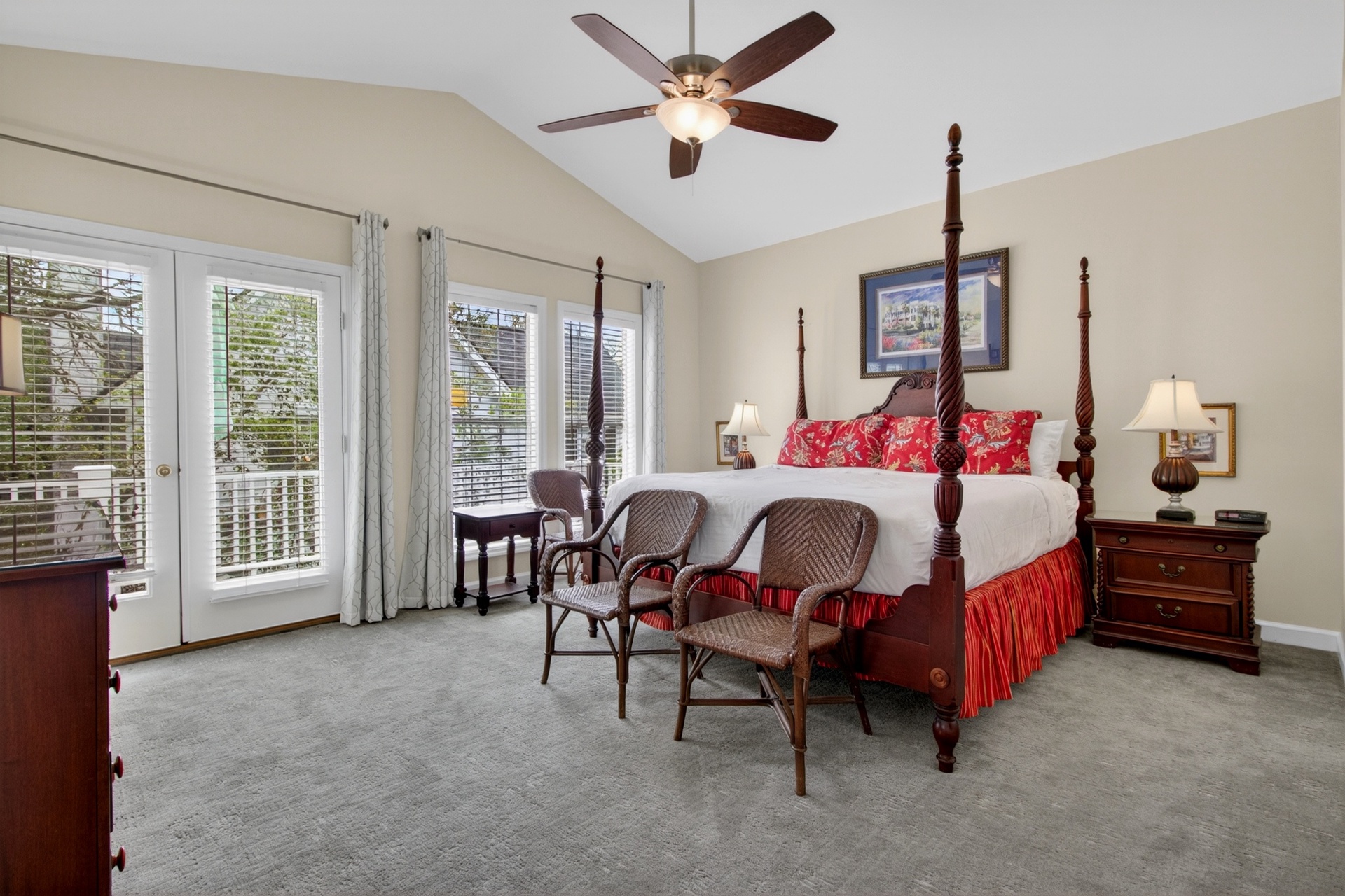 Your spacious bedroom retreat features a stunning four-poster bed with elegant red accents, vaulted ceilings with a ceiling fan, and French doors opening to your private balcony with peaceful views.