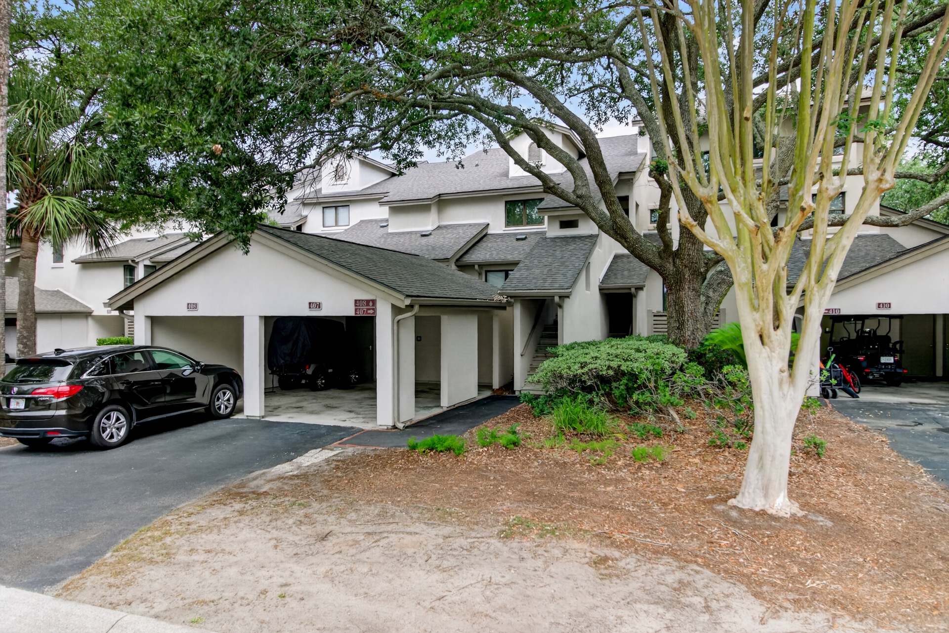 Multi-unit residential property with attached garages, landscaped with mature trees and tropical plantings, providing convenient covered parking for guests.