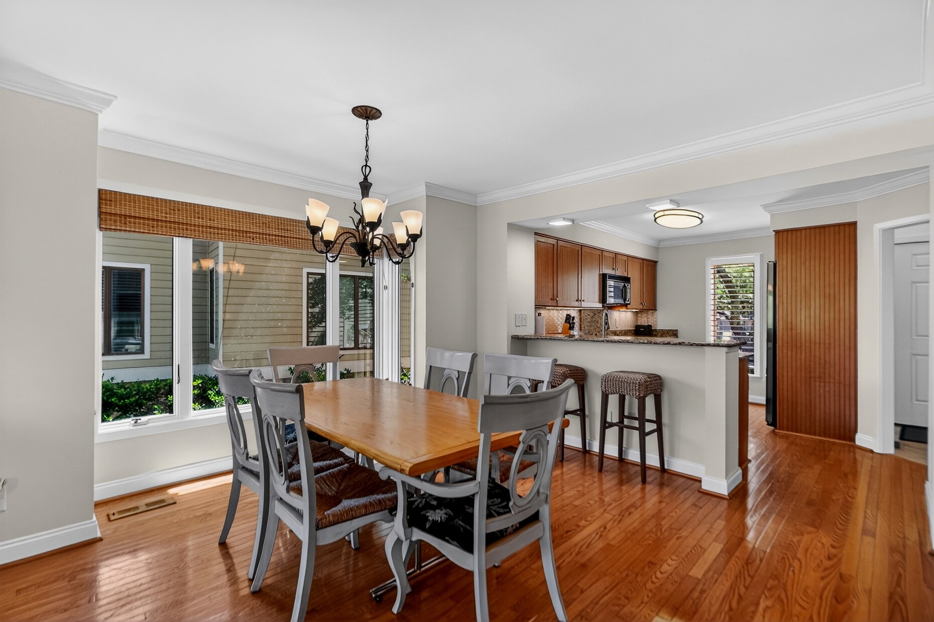 Your open-concept dining and kitchen space features gleaming hardwood floors, a breakfast bar for casual meals, and abundant natural light streaming through floor-to-ceiling windows overlooking the lush greenery outside.