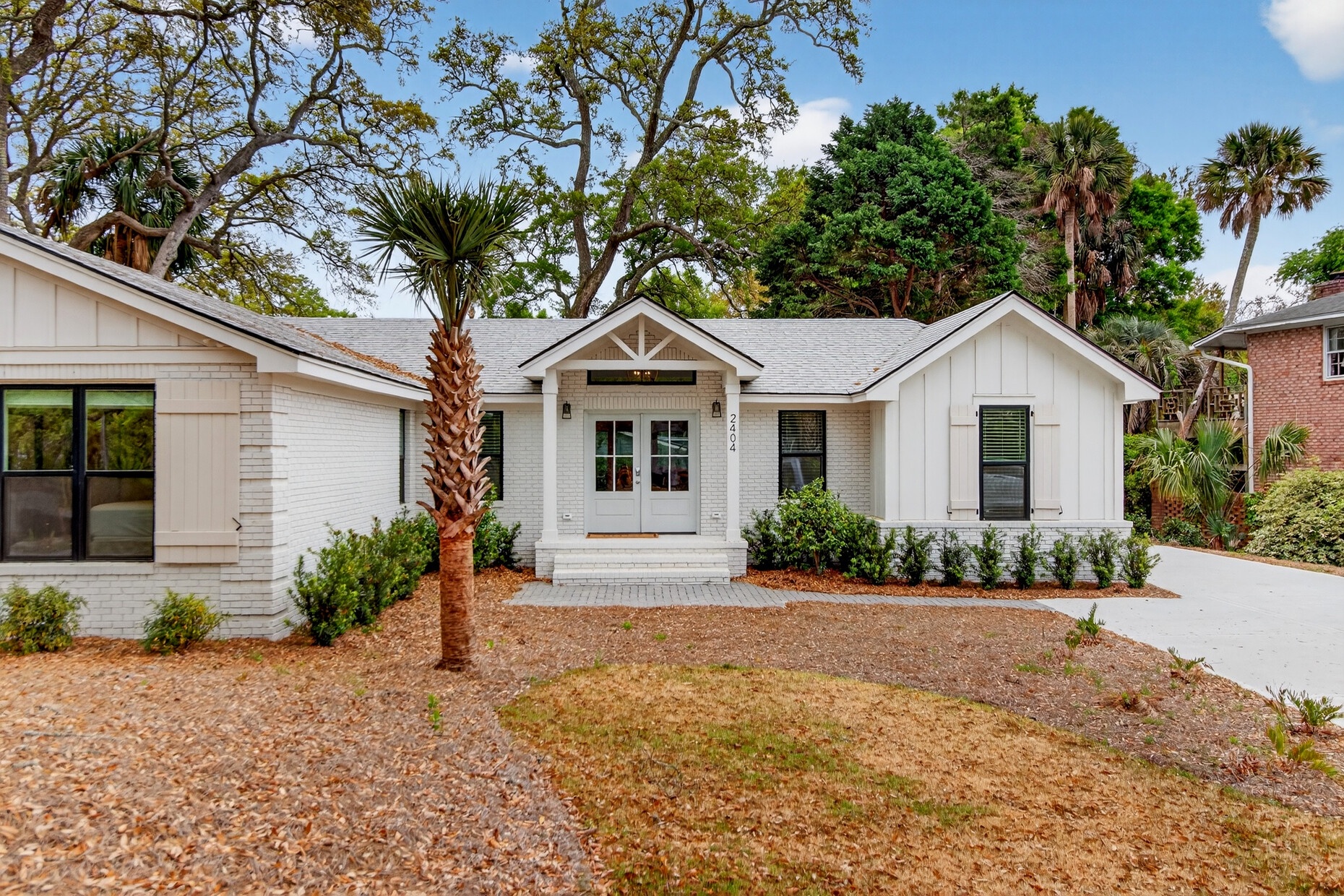 Modern coastal cottage nestled among mature palms and lush landscaping in a peaceful residential setting.