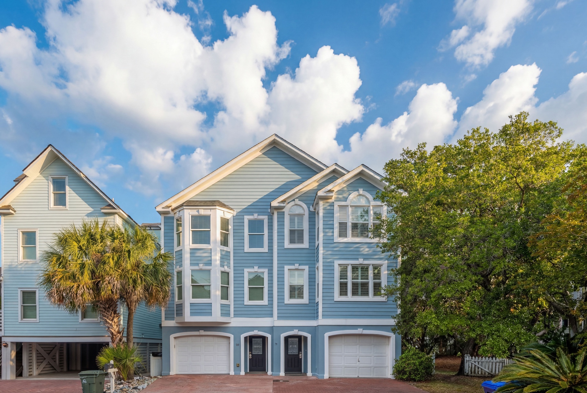 Coastal-style architecture welcomes guests with charming blue siding and white trim, set against swaying palms and a bright Carolina sky.