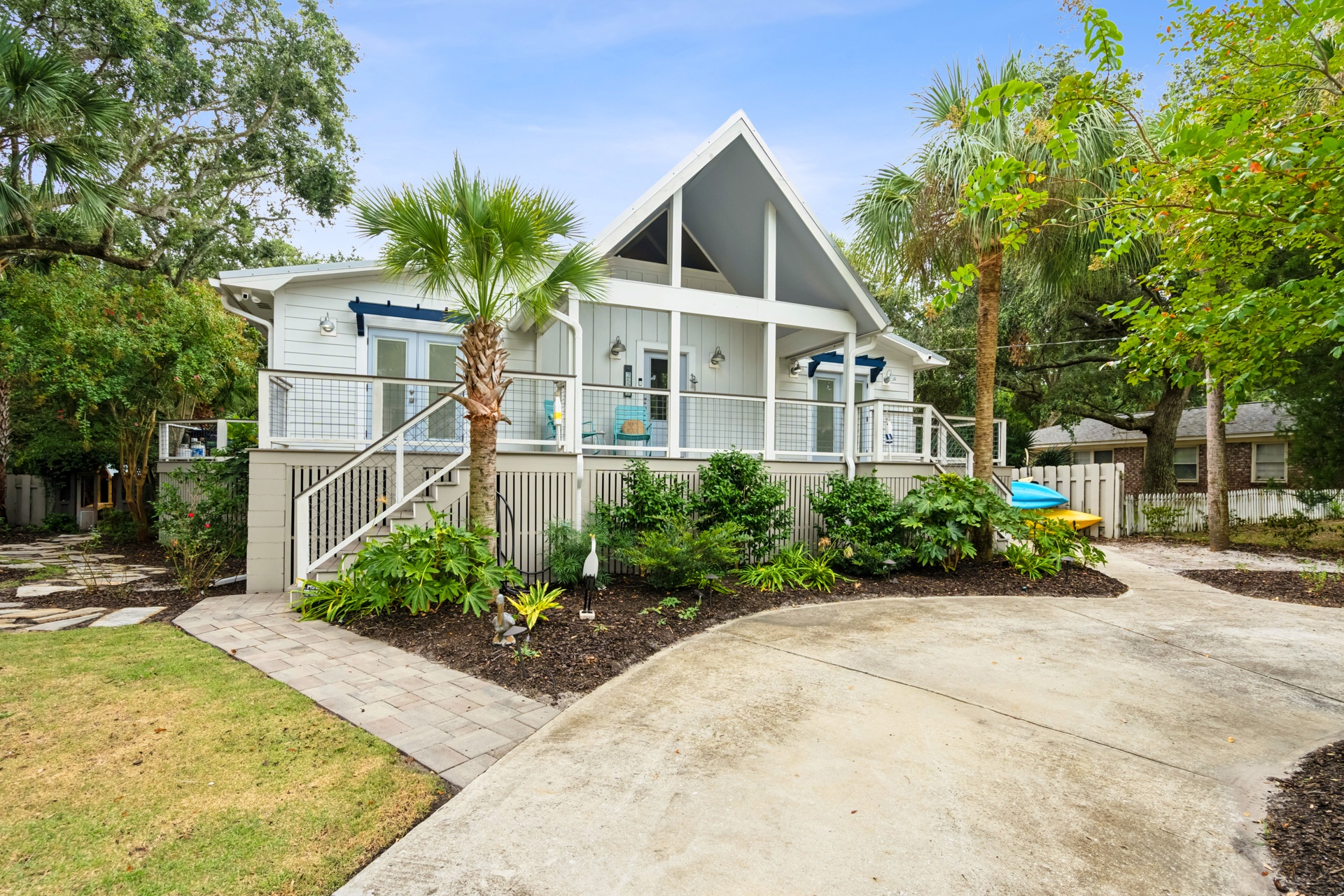 A charming coastal cottage with a peaked roof design, surrounded by lush tropical palms and native landscaping, welcoming guests to a peaceful retreat setting.