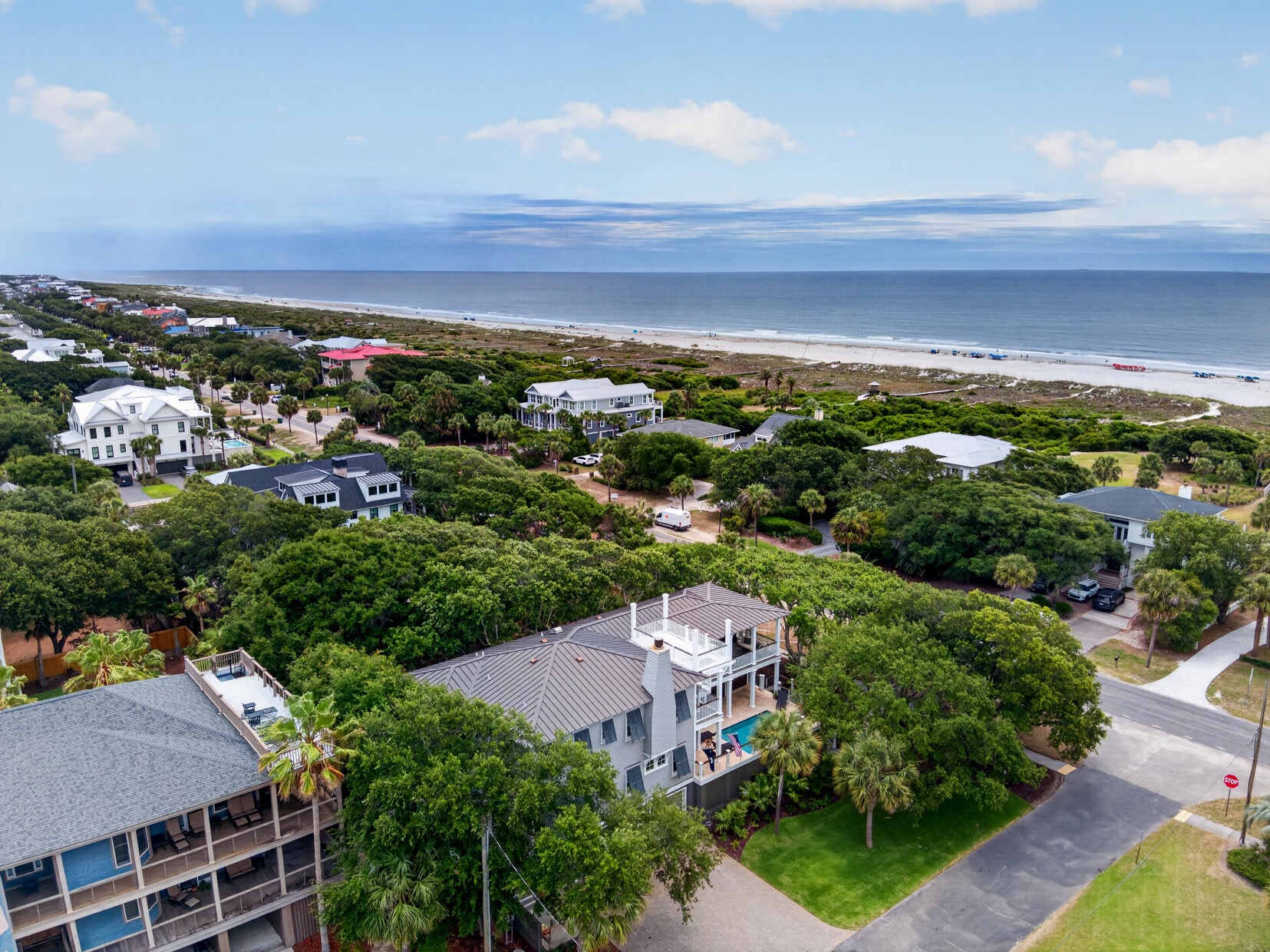 Aerial view of coastal vacation properties nestled among lush greenery with pristine beach and ocean stretching beyond, showcasing the peaceful seaside neighborhood setting.