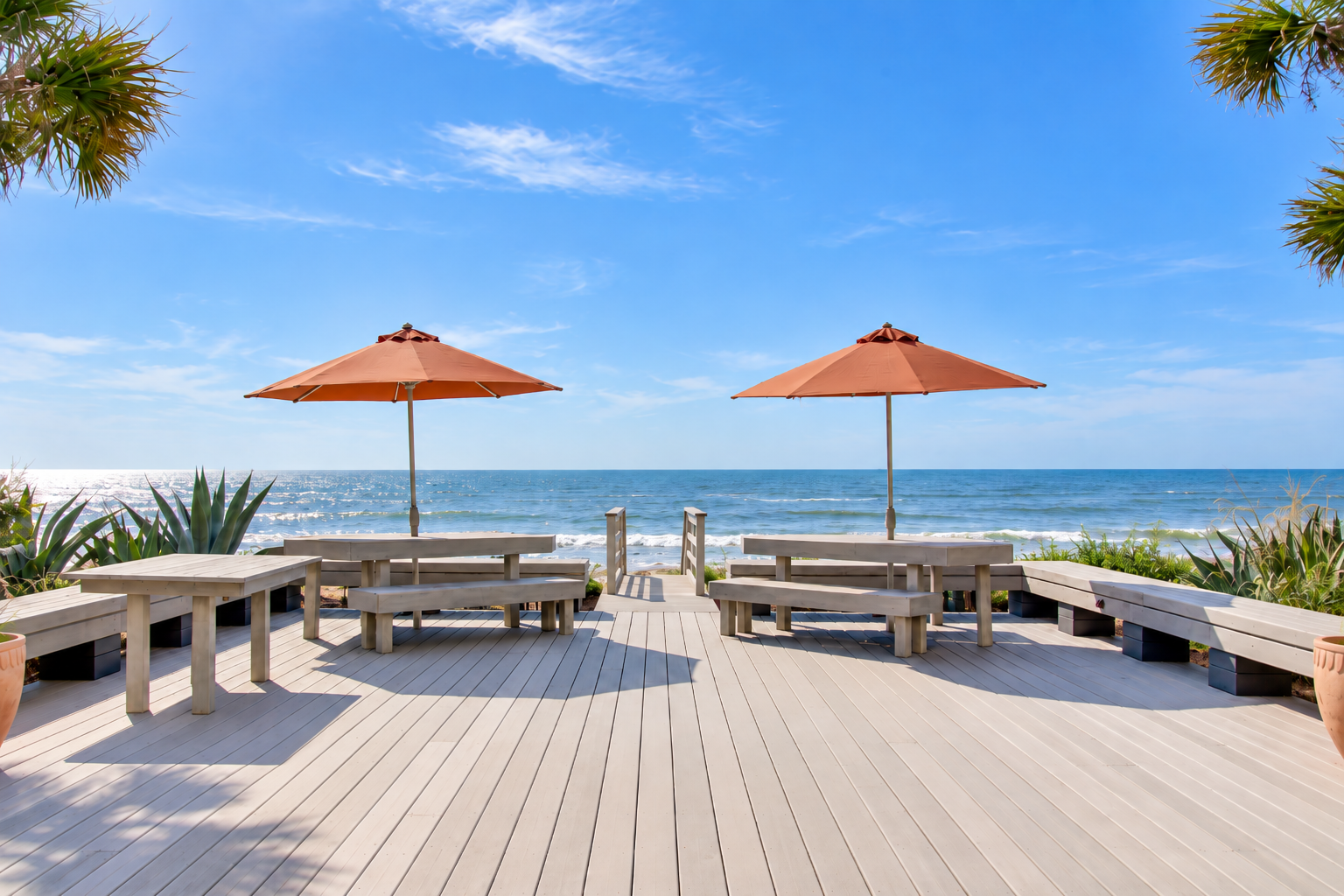 The property features a beachfront deck overlooking the ocean, with loungers and umbrellas for guests to enjoy sunny days by the shore.