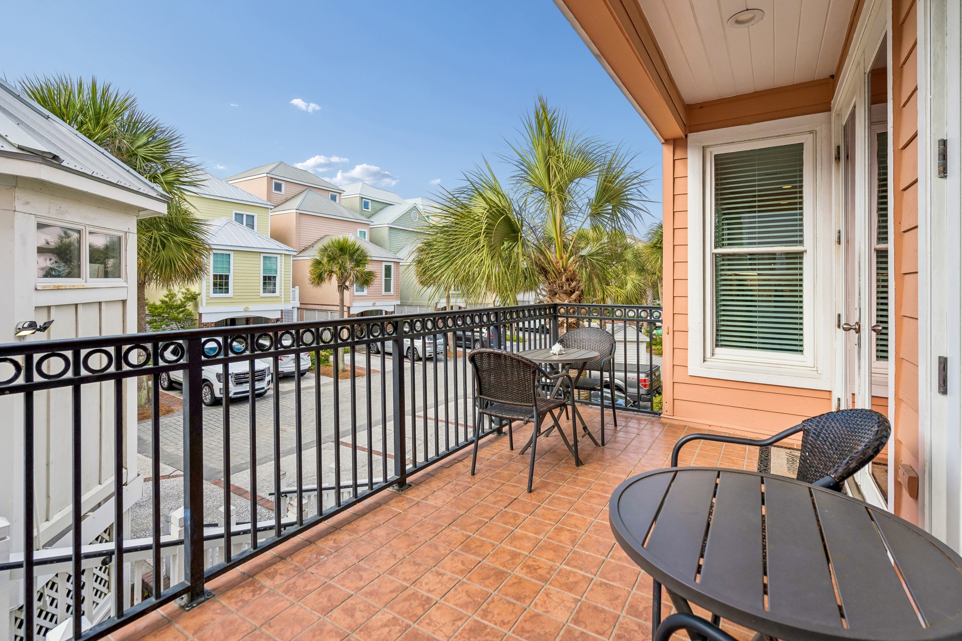 Step onto your private balcony with charming bistro seating, where tropical palms frame colorful neighborhood views under endless blue skies.
