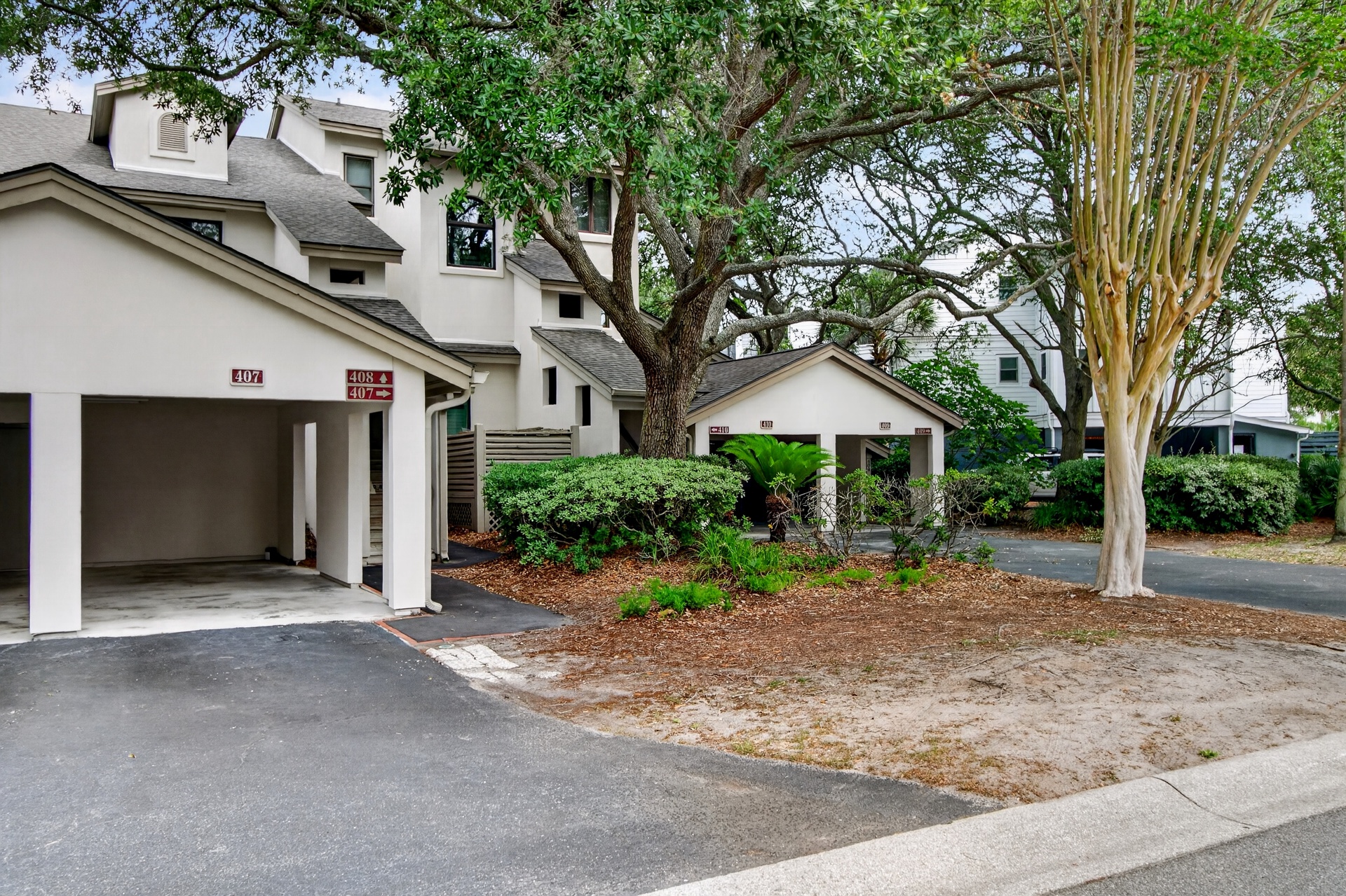 A residential complex featuring numbered units with covered carports, set among mature trees and landscaped grounds with convenient parking areas.