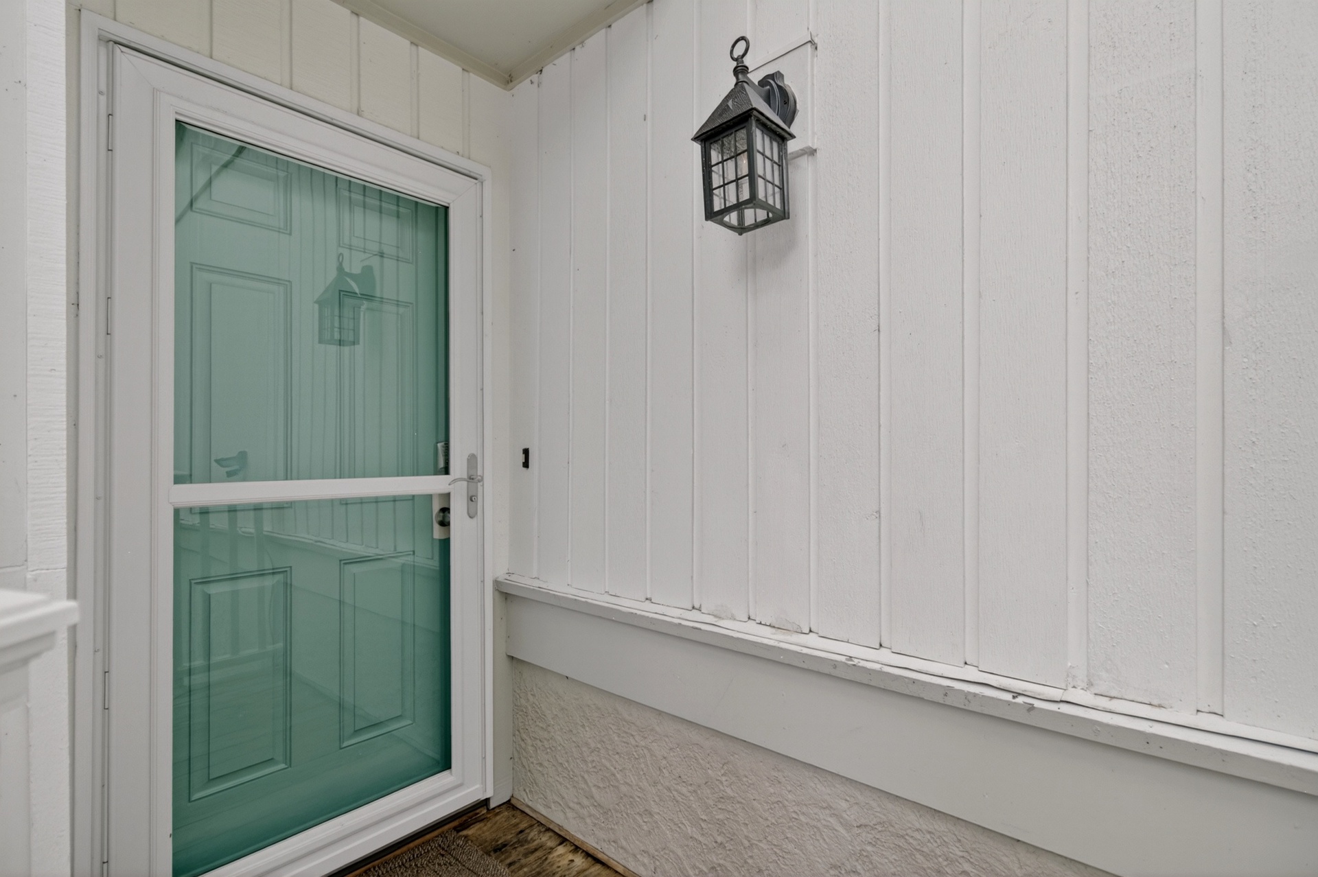 Clean, white exterior with a welcoming turquoise door and classic lantern, marking the entrance to the property.