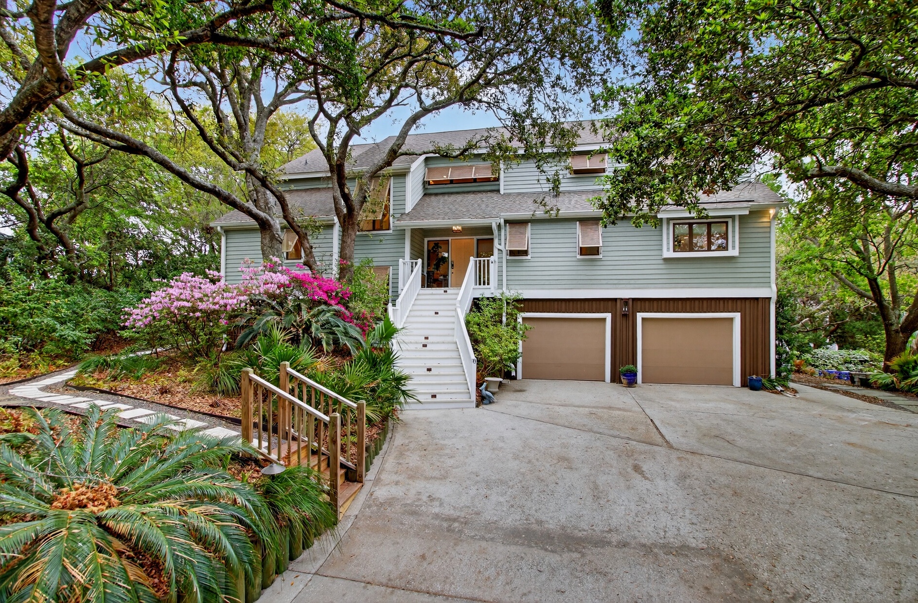 A charming coastal home nestled among mature trees with vibrant azaleas and tropical landscaping greeting your arrival.