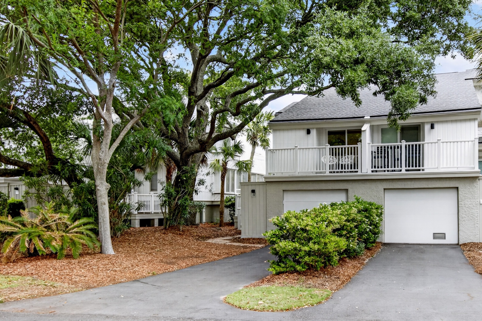 A coastal retreat framed by majestic oak trees and lush landscaping, featuring covered balconies and a two-car garage amid a peaceful residential setting.