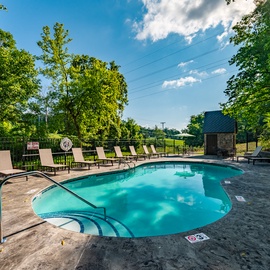 A welcoming outdoor pool area surrounded by lush greenery, offering loungers and shaded seating for your sunny afternoons. Perfect for cooling off and soaking up the peaceful summer atmosphere.