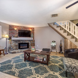 Relax in your spacious living room featuring exposed brick fireplace, cozy seating, and rustic wooden staircase leading to your private upstairs retreat.