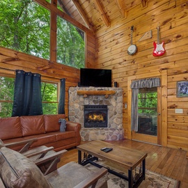 Unwind in this cozy living room where warm wood surrounds you, a stone fireplace crackles with welcoming heat, and floor-to-ceiling windows frame lush forest views. Your peaceful retreat awaits.