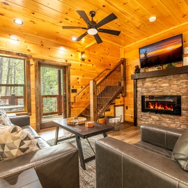 Cozy up in your rustic living room with warm wood walls, crackling fireplace, and forest views through picture windows.