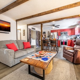 Cozy up in your mountain lodge living room with rustic beams, plush seating, and a vibrant red kitchen ready for cooking adventures.