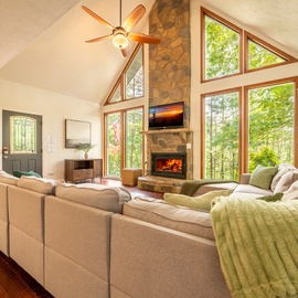 Unwind in your sunlit living room with soaring cathedral ceilings, a cozy stone fireplace, and floor-to-ceiling windows framing tranquil forest views—your perfect retreat after a day of adventure.