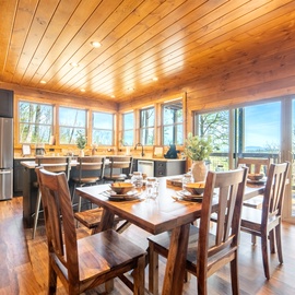Your open-concept dining room flows seamlessly into the kitchen, where warm wood tones and panoramic windows create the perfect space for memorable meals.
