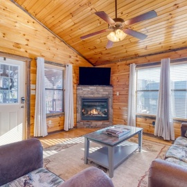 Cozy up in your rustic living room with crackling fireplace, warm wood walls, and comfortable seating for perfect mountain cabin relaxation.