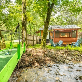 Nestled among towering trees beside a gentle creek, this cozy cabin retreat offers your own private playground with swings and Adirondack chairs for peaceful afternoons outdoors.