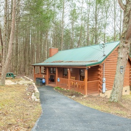 A charming log cabin nestled among towering trees, featuring a welcoming front porch and peaceful forest setting for your mountain getaway.