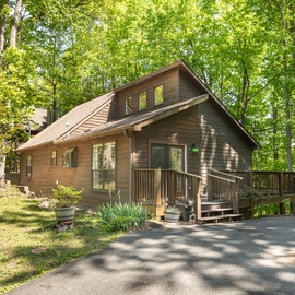 A charming wooden cabin nestled among towering trees, featuring a welcoming deck and peaceful forest setting for your mountain getaway.