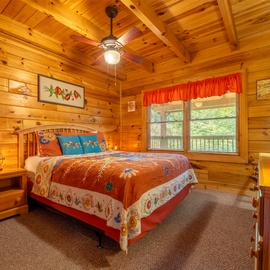 Your cozy bedroom features pine-paneled walls, vaulted wood ceilings, and charming rustic decor. Wake to soft light filtering through the windows overlooking the wooded surroundings.