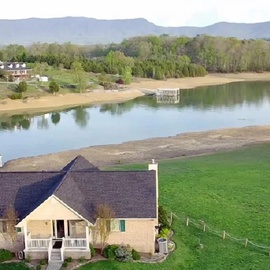 Lakefront property with peaceful waters and mountain backdrop, featuring private dock access and expansive green lawns.
