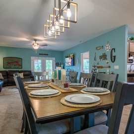 Gather around your spacious dining table beneath a modern chandelier, sharing stories and home-cooked meals in this bright, coastal-inspired open living space. The nautical touches and calming teal hues invite you to relax and make memories together.